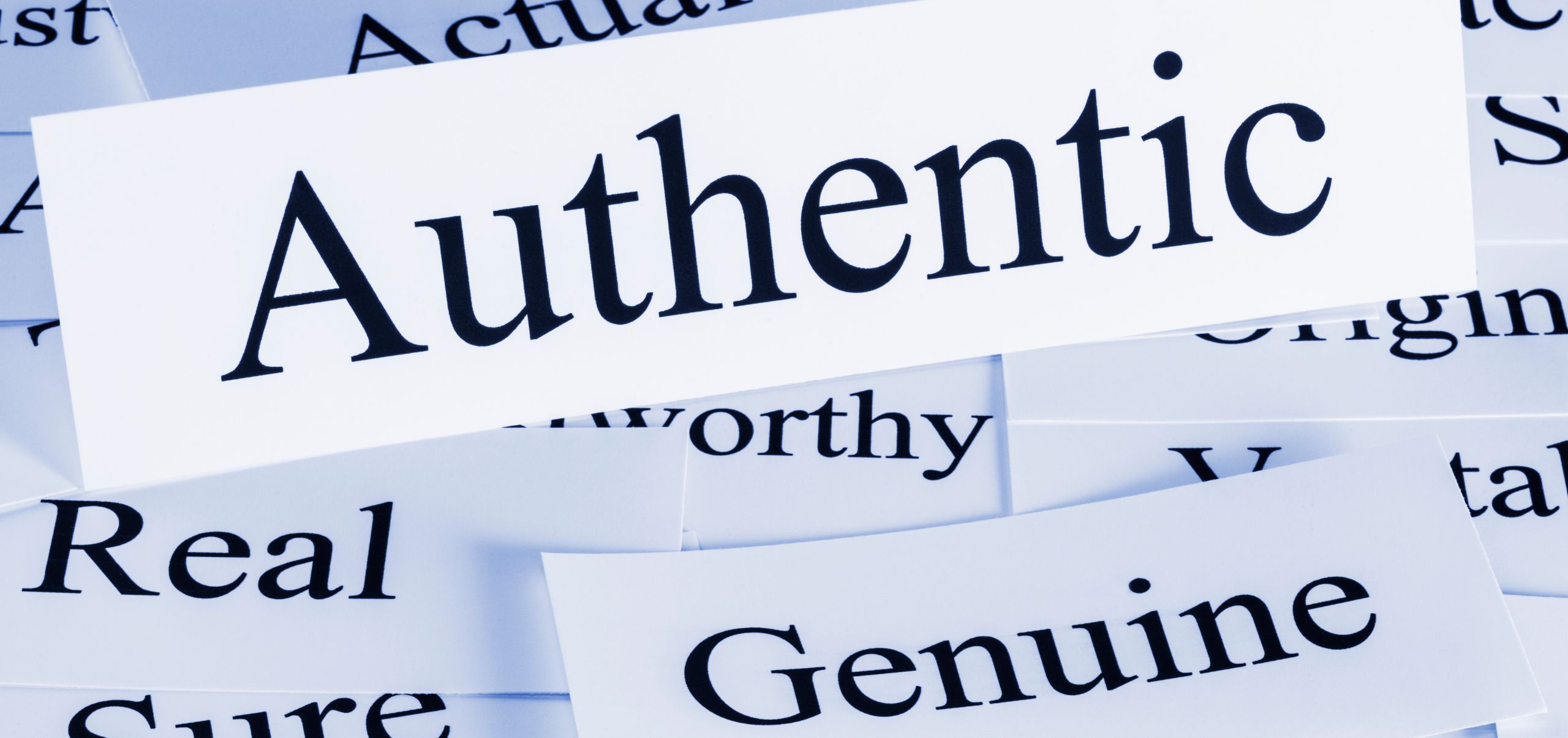 Multiple small papers with words like real, genuine, sure, and AUTHENTICITY most visible, highlighting authenticity as a key brand trait
