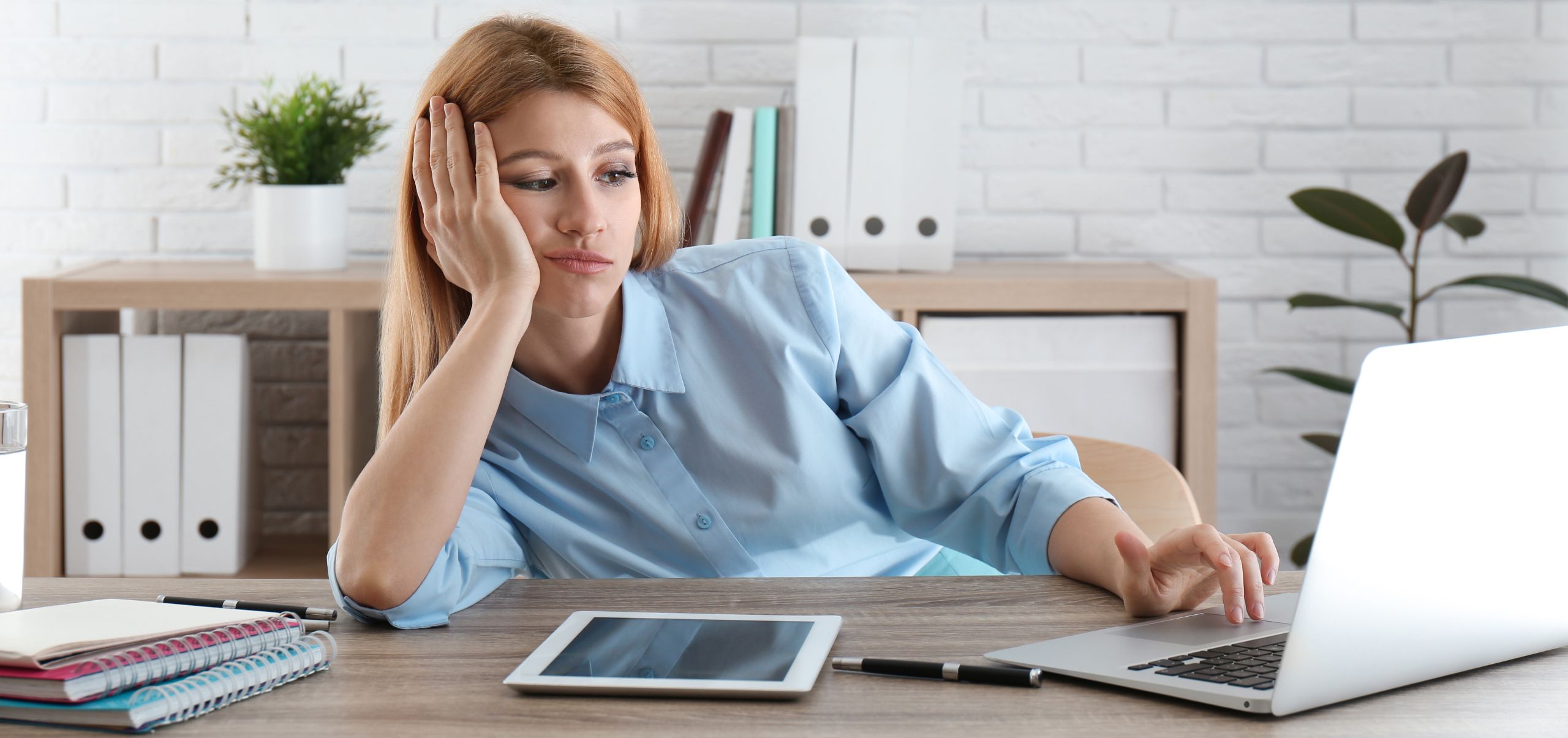 Woman looking tired and bored at her laptop, illustrating wasted time