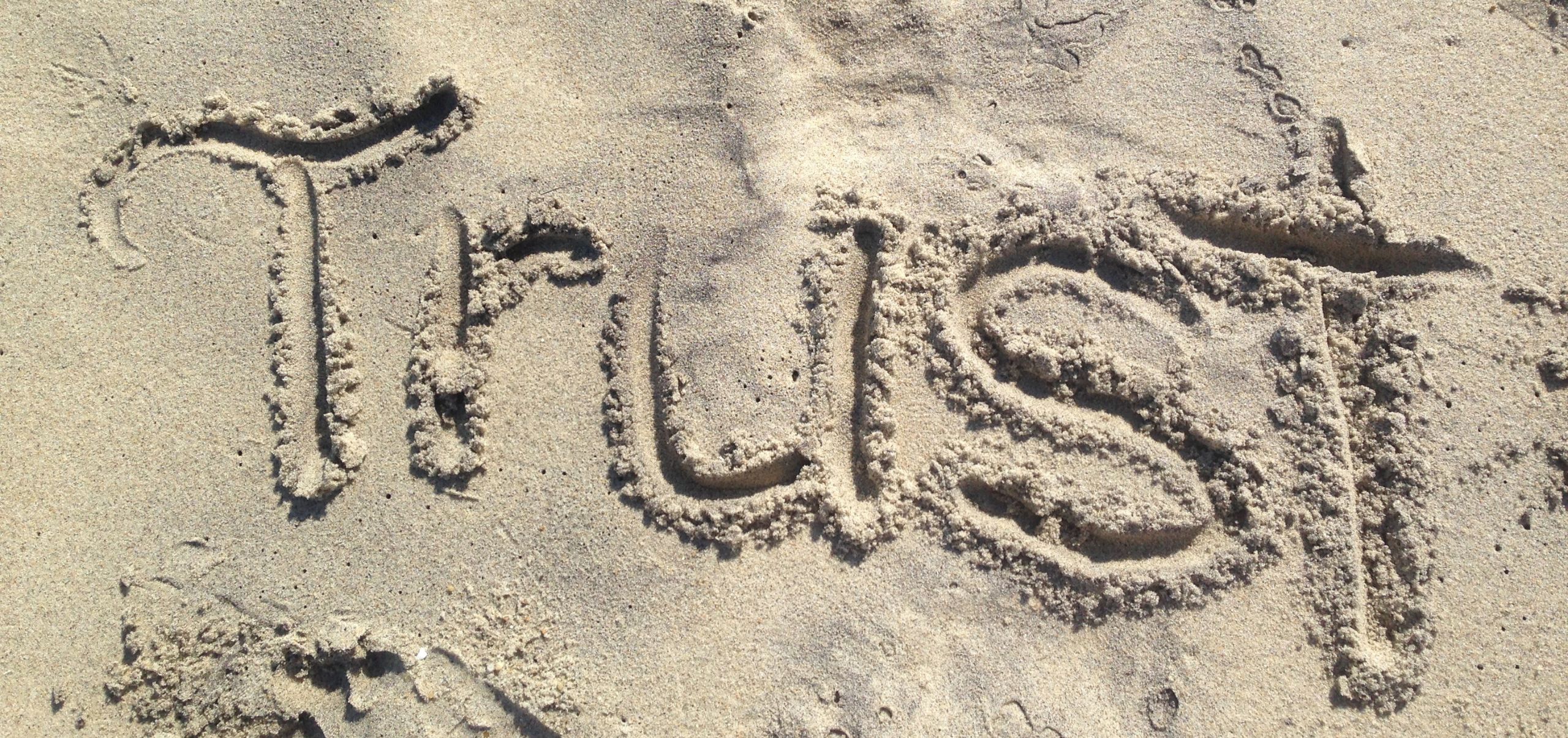The word “Trust” written on sand