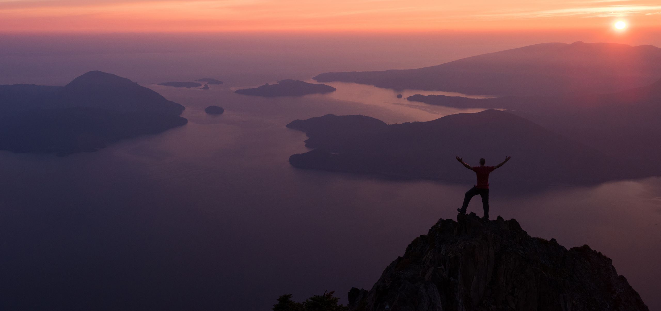 Person on a mountain at sunset with hands raised showing achievement and purpose