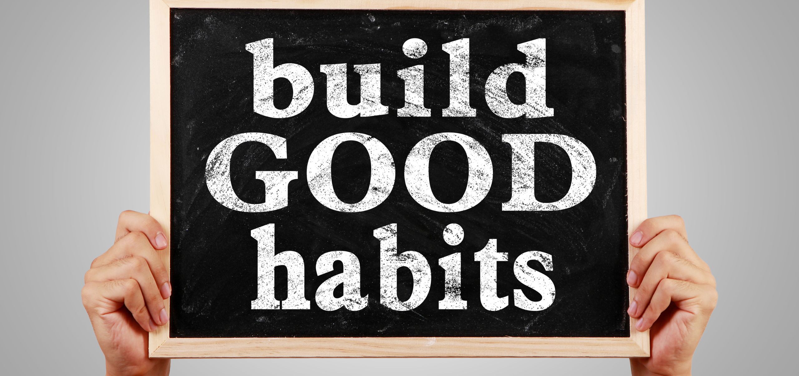 Person holding a chalkboard that says “Build Good Habits”, showing routines for time management