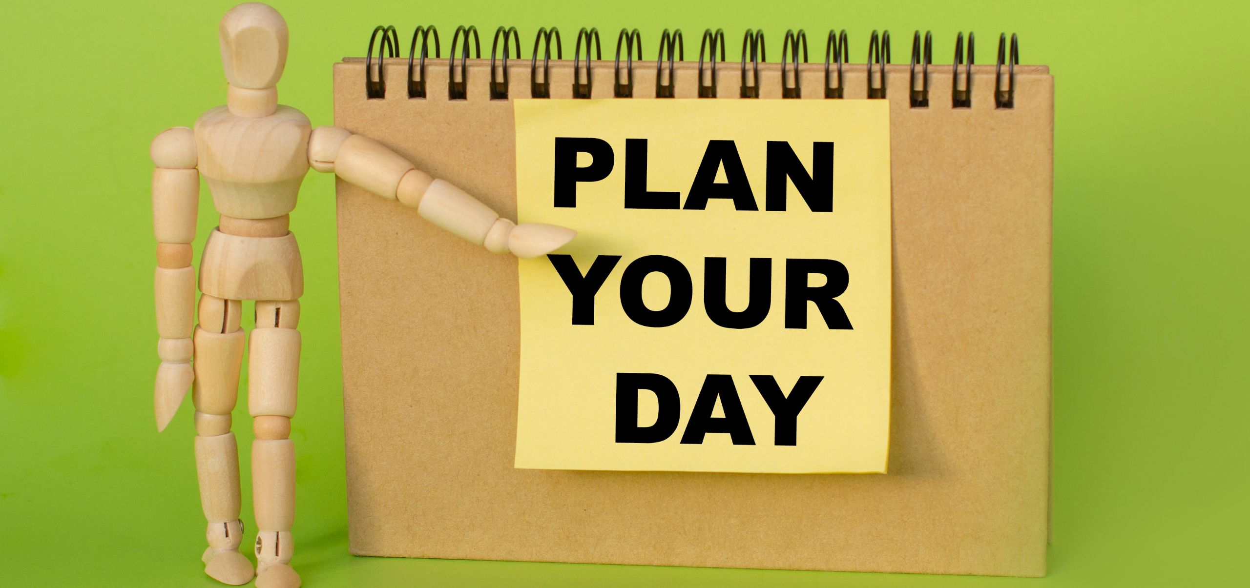 Small wooden figure pointing at a paper that says “Plan Your Day,” showing daily planning for better time management