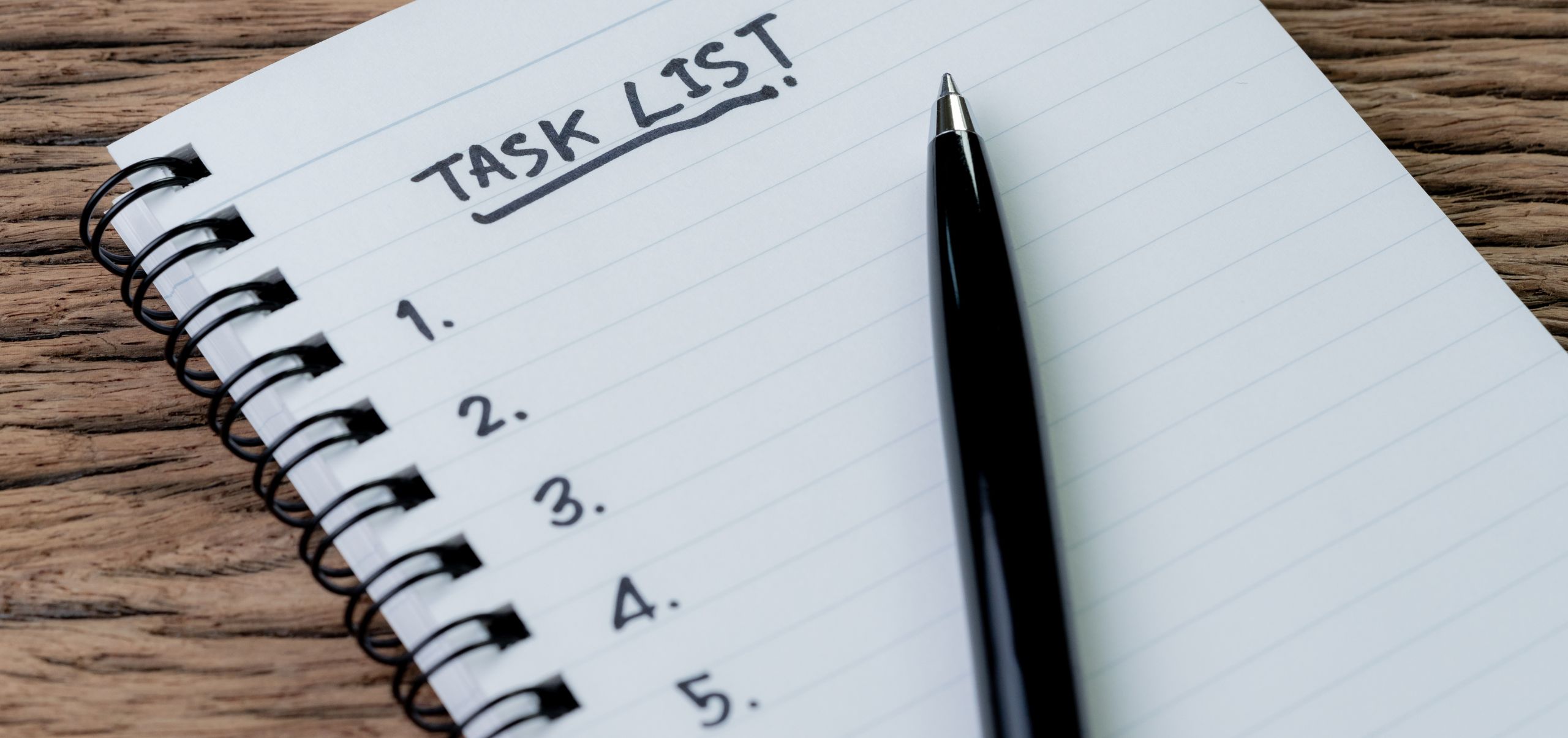 Open journal on a table with “Task List” written and a pen lying on the page