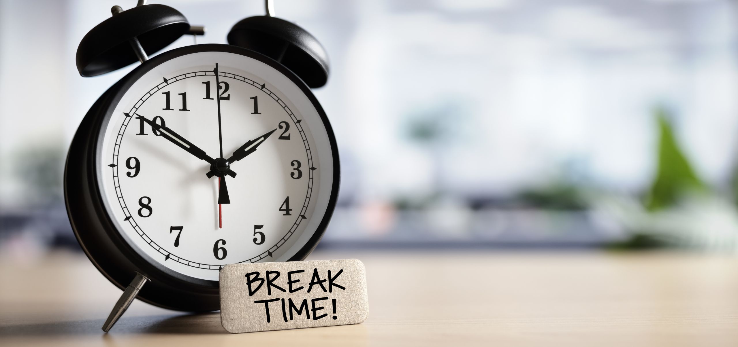 Black alarm clock on a table with a small block labeled “Break Time,” showing scheduled rest