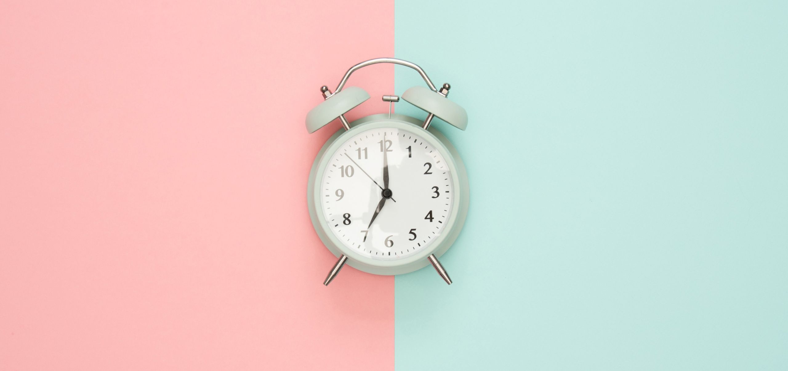 White alarm clock on a surface with pink and blue background, representing timing in email sending