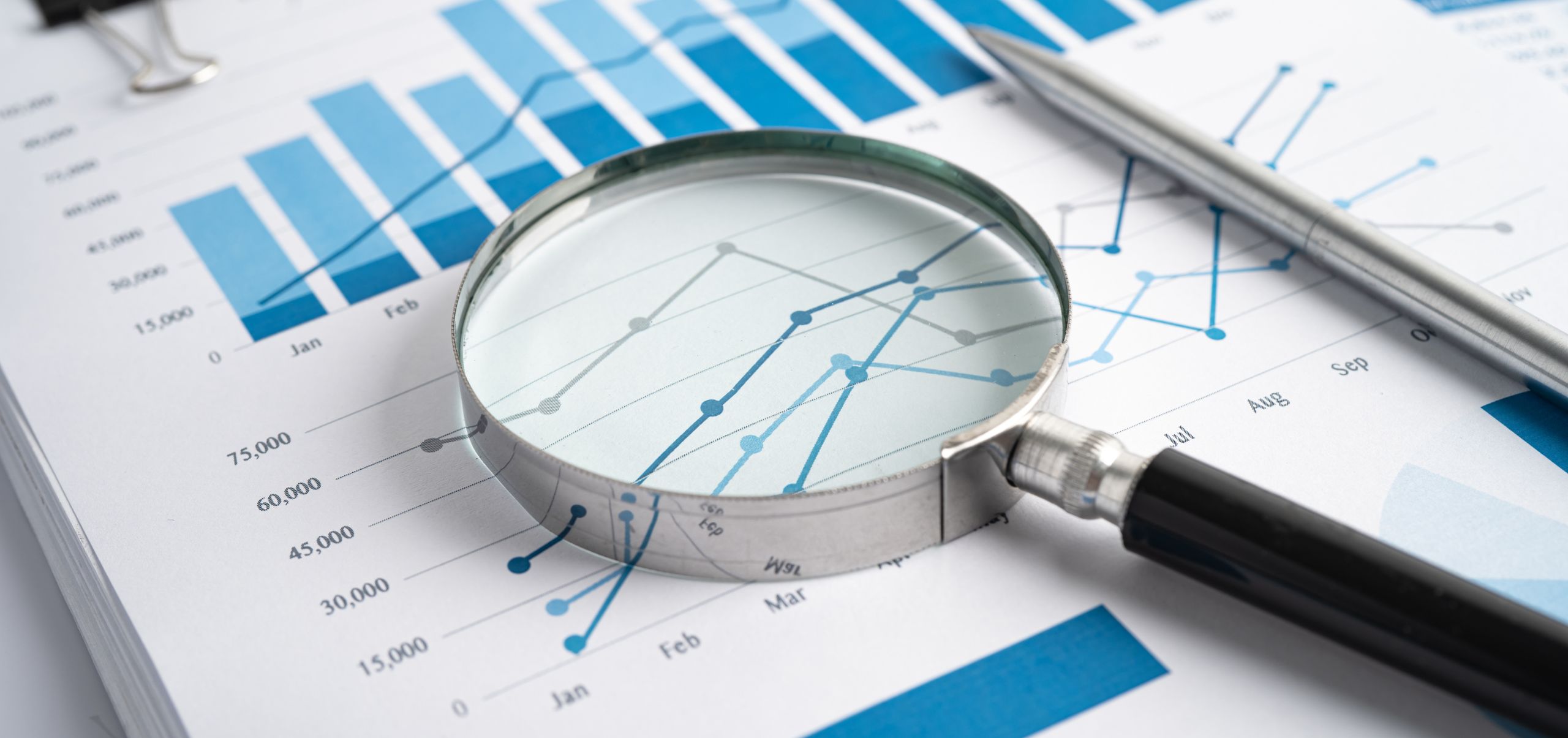 Magnifying glass over a paper with bar charts and trend lines for market research